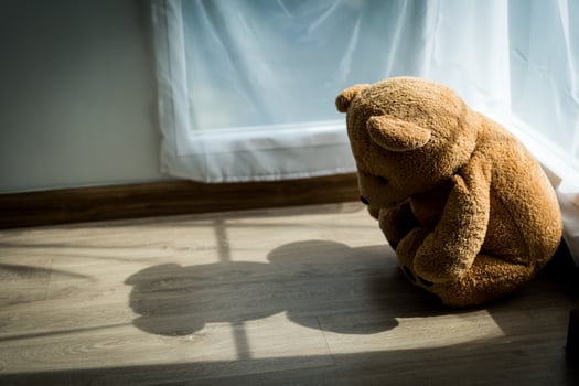 The teddy bear looked sad and disappointed sitting in the corner of the room. The teddy bear seems lonely in a room with sunlight. concept depression in children photo