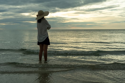 Woman wearing a hat walks alone on an empty sandy beach at sunset. A lonely and depressed young woman stands on the sand of the beach on holiday. photo