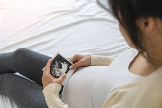 A pregnant woman is looking at an ultrasound photo of fetus. Mother gently touches the baby on stomach.Women are pregnant for 30 weeks. first love in belly and Last term pregnancy