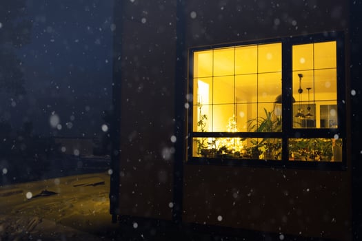 Cozy festive window of the house outside with the warm light of fairy lights garlands inside - celebrate Christmas and New Year in a warm home. Christmas tree, bokeh, snow on pine trees and snowfall photo