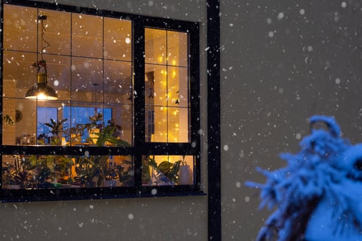 Cozy festive window of the house outside with the warm light of fairy lights garlands inside - celebrate Christmas and New Year in a warm home. Christmas tree, bokeh, snow on pine trees and snowfall photo