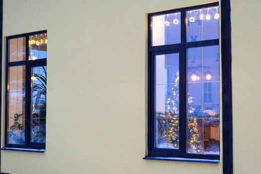 Cozy festive window of the house outside with the warm light of fairy lights garlands inside - celebrate Christmas and New Year in a warm home. Christmas tree, bokeh, snow on pine trees and snowfall photo