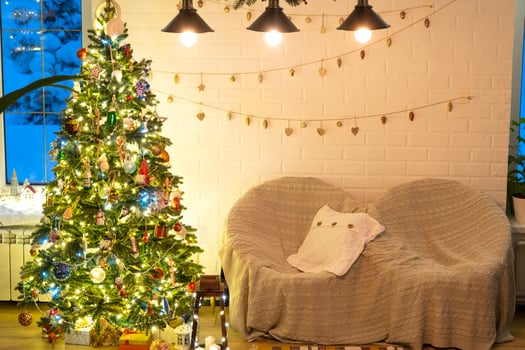 Christmas tree in white interior of a house with loft-style brick walls with garlands of glass toys on a rope. Glowing fairy lights decoration of the studio room. Cozy home in christmas and new year photo
