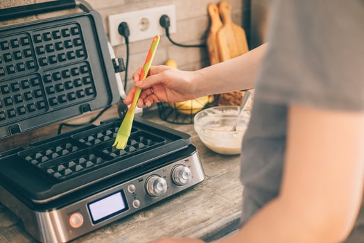 Young woman preparing Belgian waffles in the kitchen, greasing the waffle iron with coconut oil. Cooking process photo