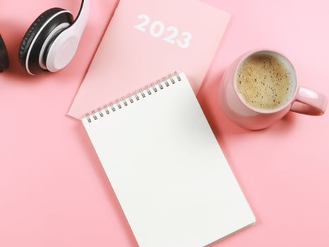 flat lay of blank paper note book on pink diary or planner 2023, headphones and pink cup of coffee on pink background with copy space. photo