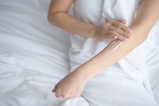 Asia woman sitting on bed and applying cream on body. photo