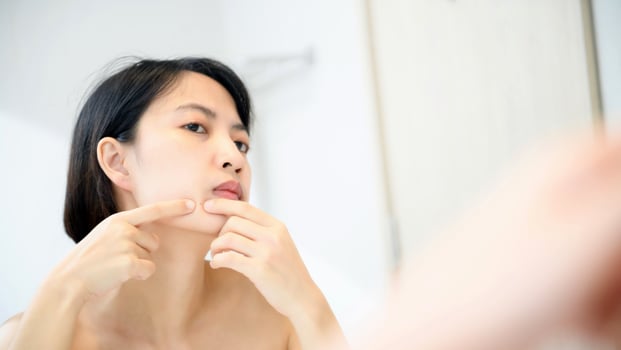 Problem skin. Concerned young asian women popping pimple on cheek while standing near mirror in bathroom. young asian women with acne photo