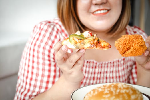 An Asian fat woman is eating pizza and fried chicken on the sofa in her house. The concept of consuming food that causes disease is not good for health photo