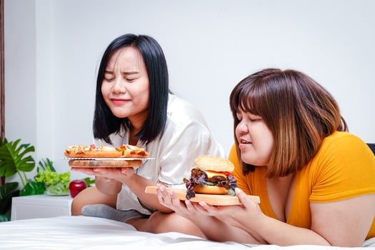 Two fat girls eat pizza and hamburgers in bed in the bedroom. Happy. The concept of eating and health care. photo