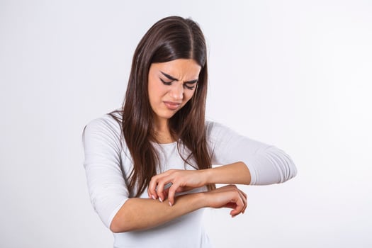 Young woman scratching her arm due to itching on a gray background. Female has an itching arm. The concept of allergy symptoms and healthcare photo