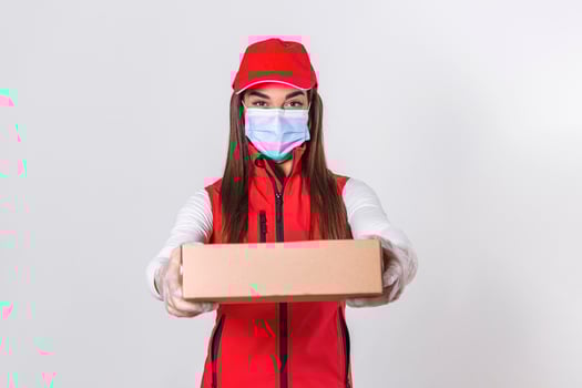 Young delivery woman in medical mask holding and carrying a cardbox isolated on white background. Buy food online in quarantine concept. photo