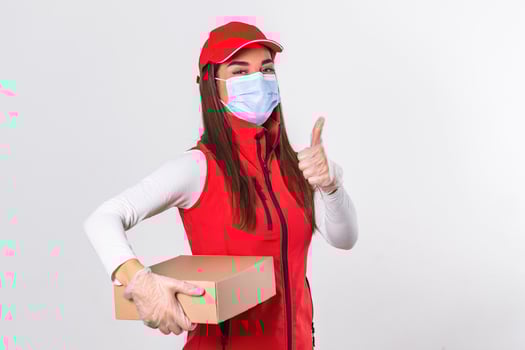 Delivery woman employee in red cap blank t-shirt uniform face mask gloves hold cardboard box showing thumbs up isolated on white background. Quarantine pandemic coronavirus virus 2019-ncov concept photo