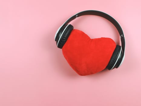 flat lay of red heart pillow coverd with headphones on pink background. Love songs or podcast concept. photo