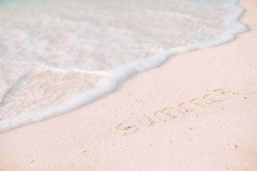 Word Summer handwritten on sandy beach with soft ocean wave on background photo