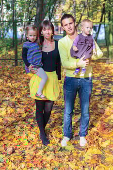 Young charming family of four walking in yellow autumn park photo