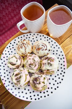Two cups of black tea stand on a wooden tray. Fresh and fragrant cinnamon rolls close up lie on a plate with polka dots, beautiful morning. Close-up. Romantic morning. View from above photo