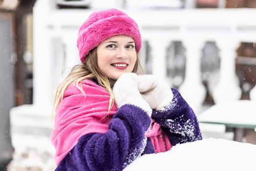 Portrait of a smiling young woman in a bright pink scarf and hat, white mittens and a purple fur coat outdoors in a city park in winter. photo