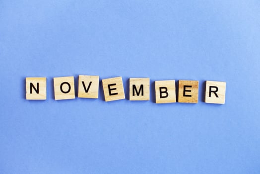inscription November made by wooden cubes on a veri peri purple background. photo