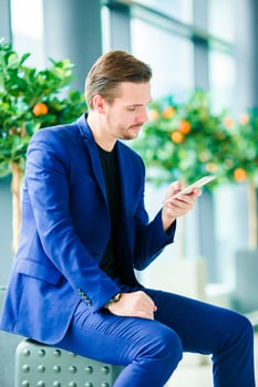 Urban businessman talking on smart phone inside in airport. Casual young boy wearing suit jacket. Caucasian man with cellphone at the airport while waiting for boarding photo