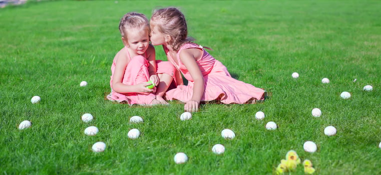 Older sister kissing younger on a green glade of Easter Eggs photo