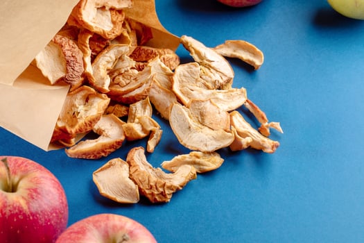 Paper bag with dispersed dried apple slices and whole fruits on blue background. photo