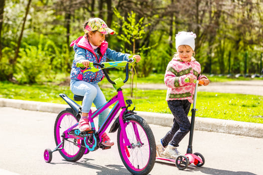 girls riding down the street on scooters and a bike photo