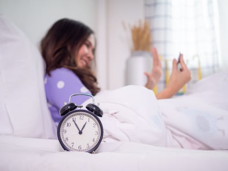 The focus image on the clock and background have The girl is using a mobile phone to chat with a video call with her boyfriend in the bedroom and sleep very late. photo