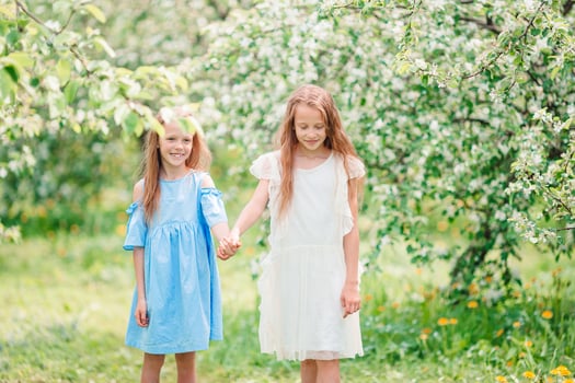 Adorable little girls in blooming apple tree garden on spring day photo