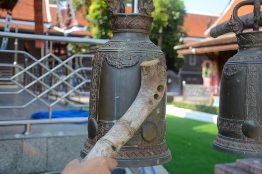 Woman hand holding a wooden hammer for bell chimes in a Buddhist temple photo