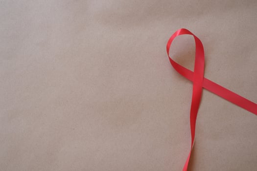 A red ribbon isolated on brown background with copyspace. Lung cancer awareness symbol for supporting people living and illness. Political movements, End violence against women campaign photo