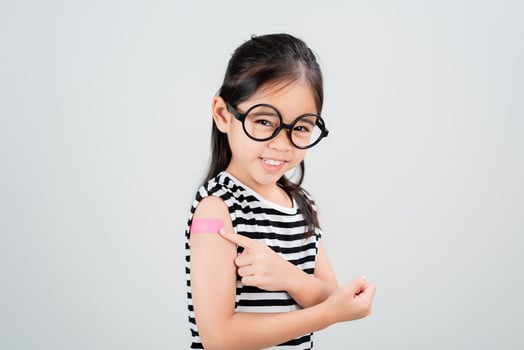 Asian little girl wear glasses showing her arm with bandage after virus vaccine happy Kid and child vaccination campaign. Protect your kid with vaccine concept photo