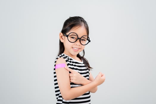 Asian little girl wear glasses showing her arm with bandage after virus vaccine happy Kid and child vaccination campaign. Protect your kid with vaccine concept photo