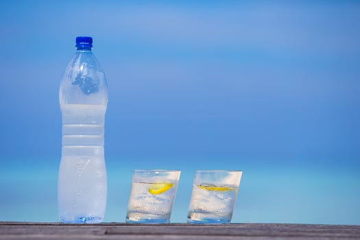 Glasses of waters with lemon and bottle on wooden on sea background photo