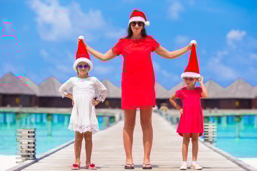 Happy mother and little girls in Santa hat near water villa on summer vacation photo