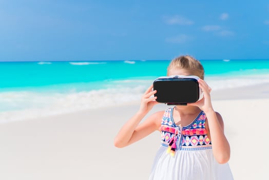 Little girl using VR virtual reality goggles. Adorable kid look into the virtual glasses on white beach photo