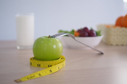 Tape measure around the green apple. Next there are milk and vegetable salad on the wooden table. Eating for good health and weight loss. Diet concept photo
