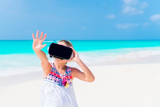 Cute little child girl using VR virtual reality goggles. Adorable girl look into the virtual glasses on white beach photo