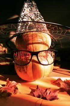 Two Halloween orange pumpkins standing one on top of other in festive bloody glasses and witch hat with spiderweb. photo