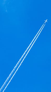 Two engined airplane during flight in high altitude with condensation trails photo