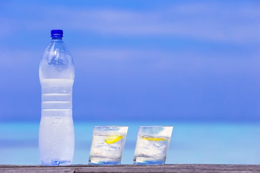 Glasses of waters with lemon and bottle on wooden on sea background photo