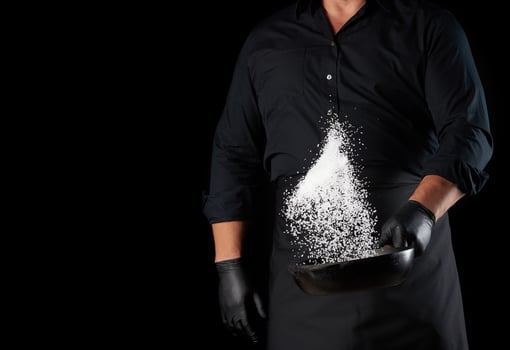 man in a black uniform holding a round cast iron pan with salt, the chef tosses white salt up photo