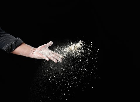 baker's male hand throws up a handful of white wheat flour on a black background photo