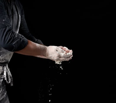 baker in black clothes holds white wheat flour in palms on black background photo
