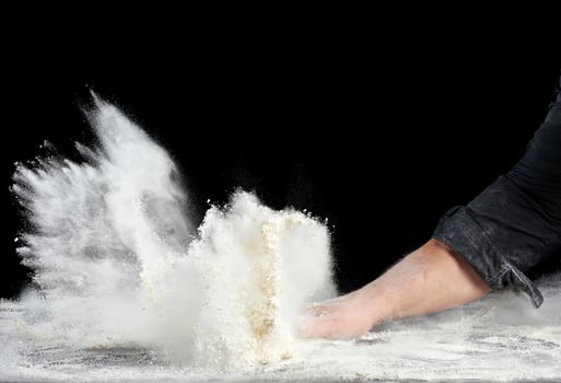 chef in black uniform sprinkles white wheat flour in different directions, product scatters dust photo