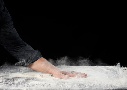 chef in black uniform sprinkles white wheat flour in different directions photo