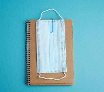 disposable medical face mask and spiral paper notepad on blue background photo