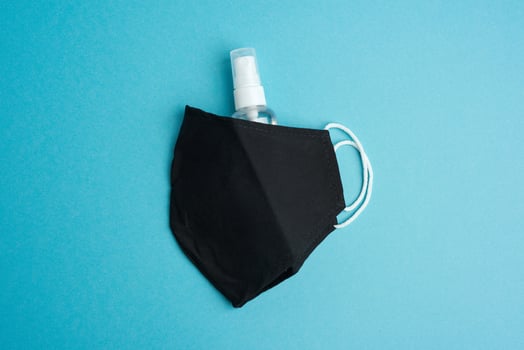 reusable black textile mask, bottle for disinfector on a blue background photo