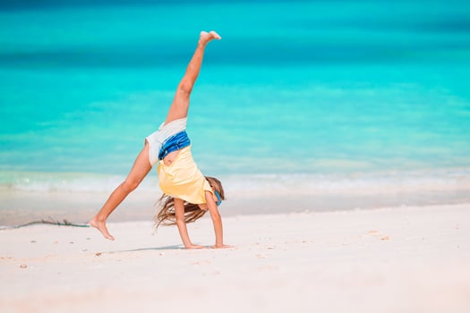 Active little girl at beach having a lot of fun. Cute kid making sporty exercises on the seashore photo