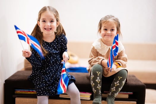 Two sisters are sitting on a couch at home with icelandic flags on hands. Iceland children girls with flag . photo