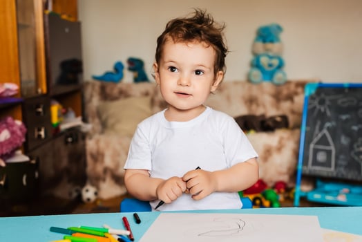 a small boy draws on sheets of paper lying on the table with colored pencils photo
